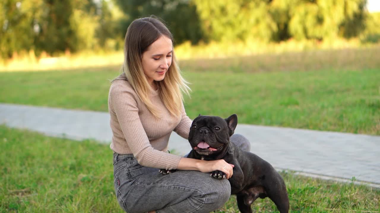 这名女子坐在从收容所救出的黑色法国斗牛犬旁边，抚摸着它。帮助无家可归的动物视频素材