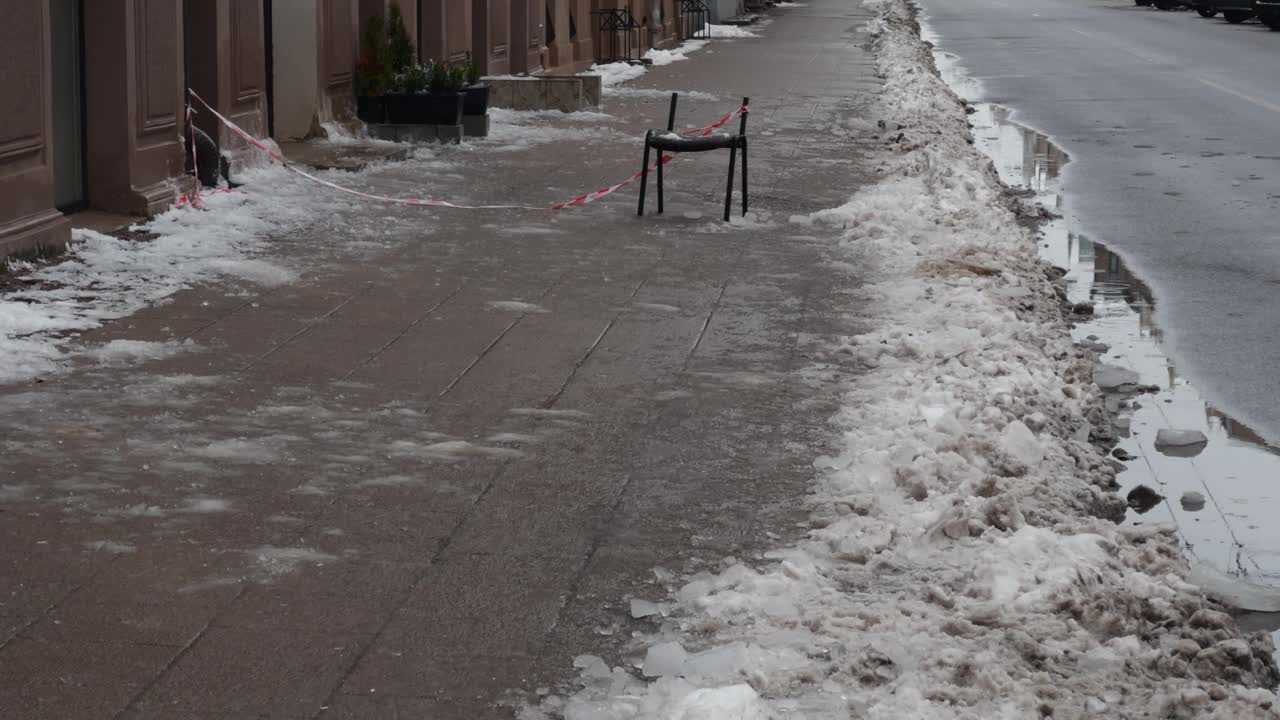 一张椅子坐在积雪的人行道上，周围是建筑物和沥青视频素材