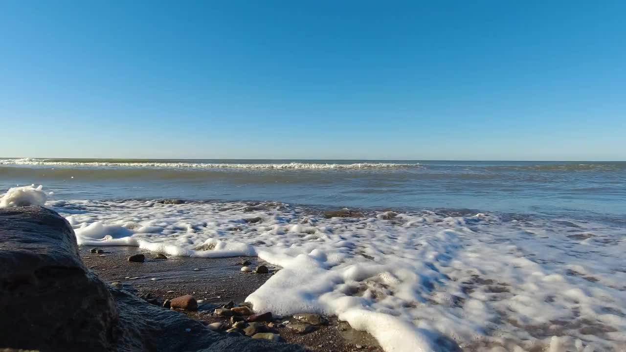 夏天:海浪冲过海滩的海岸线，岩石产生泡沫和水花。视频素材