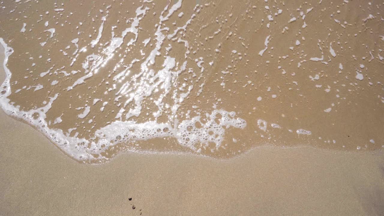 在阳光明媚的日子里，海浪平静地拍打着沙滩的海岸视频下载