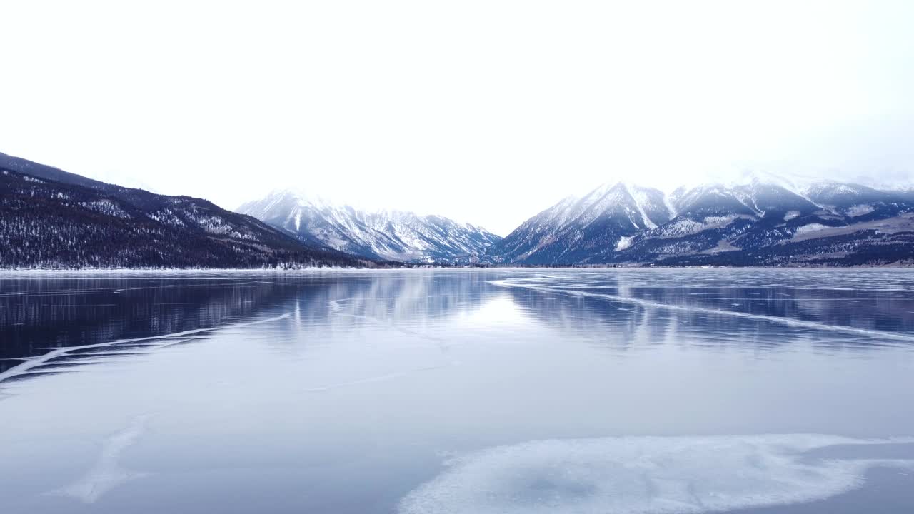 从白雪皑皑的山上飞过冰封的湖面，冰面上有裂缝视频素材