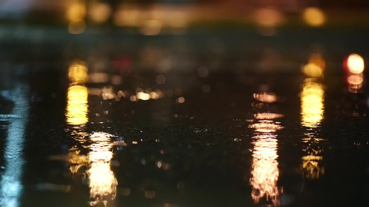 夜城暴雨的大气视频。大雨和汽车从低洼处经过的水坑溅起的水花。在街灯的照耀下，大雨滴落在人行道上视频素材