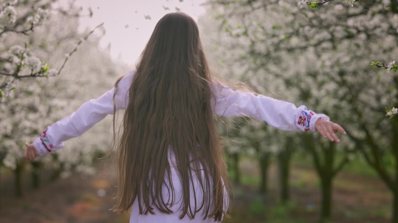 在保加利亚的一个乡村花园里，一个穿着民族民间刺绣服装的保加利亚女孩和盛开的果树视频下载