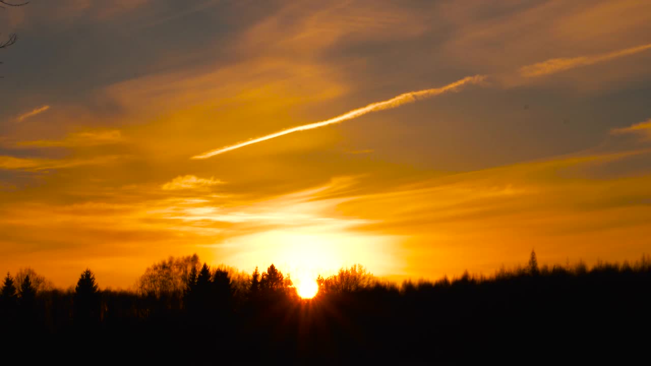 史诗般的饱和黄金小时夕阳天空与森林剪影和飞机的轨迹视频素材