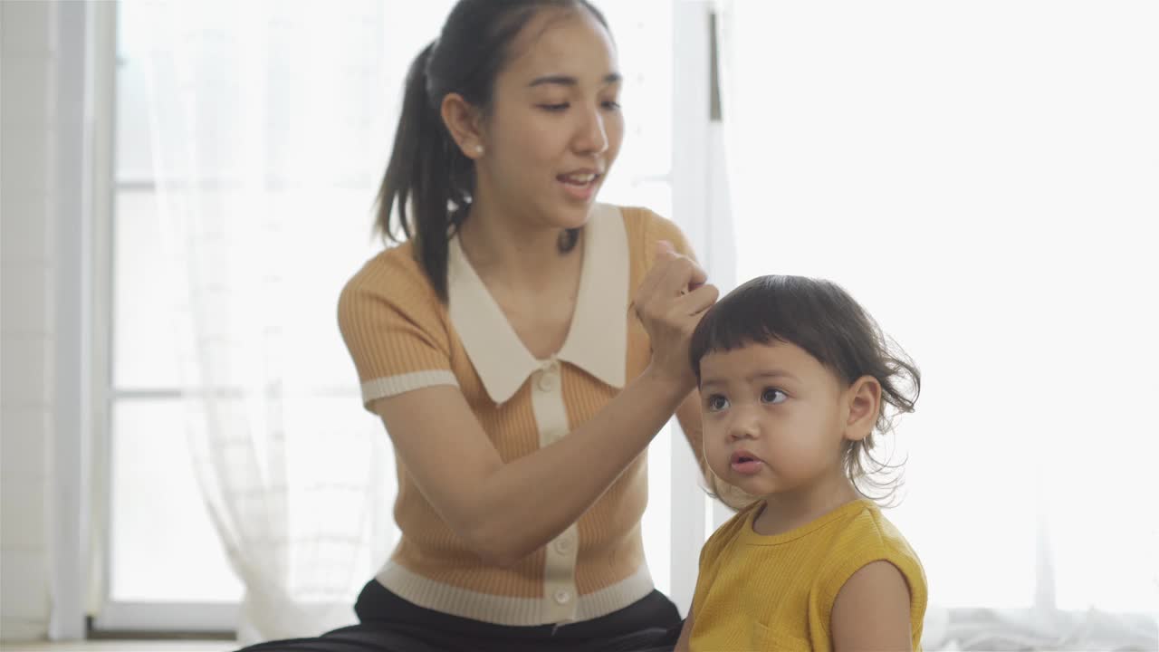 妈妈在家里给一个小女孩梳头发。视频下载