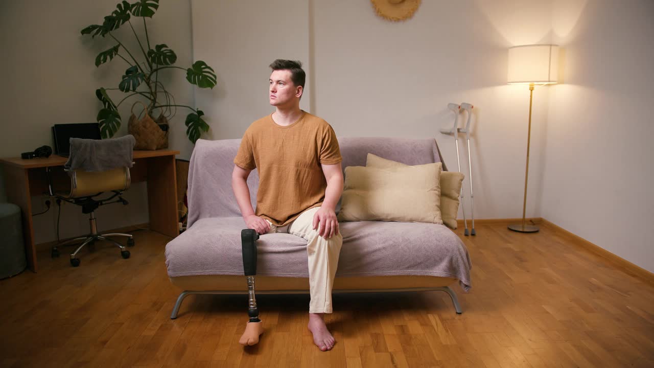 一名截肢者在家中坐着，膝盖以上的假肢残疾，经股腿假体人工装置。截肢残障人士的日常生活视频素材