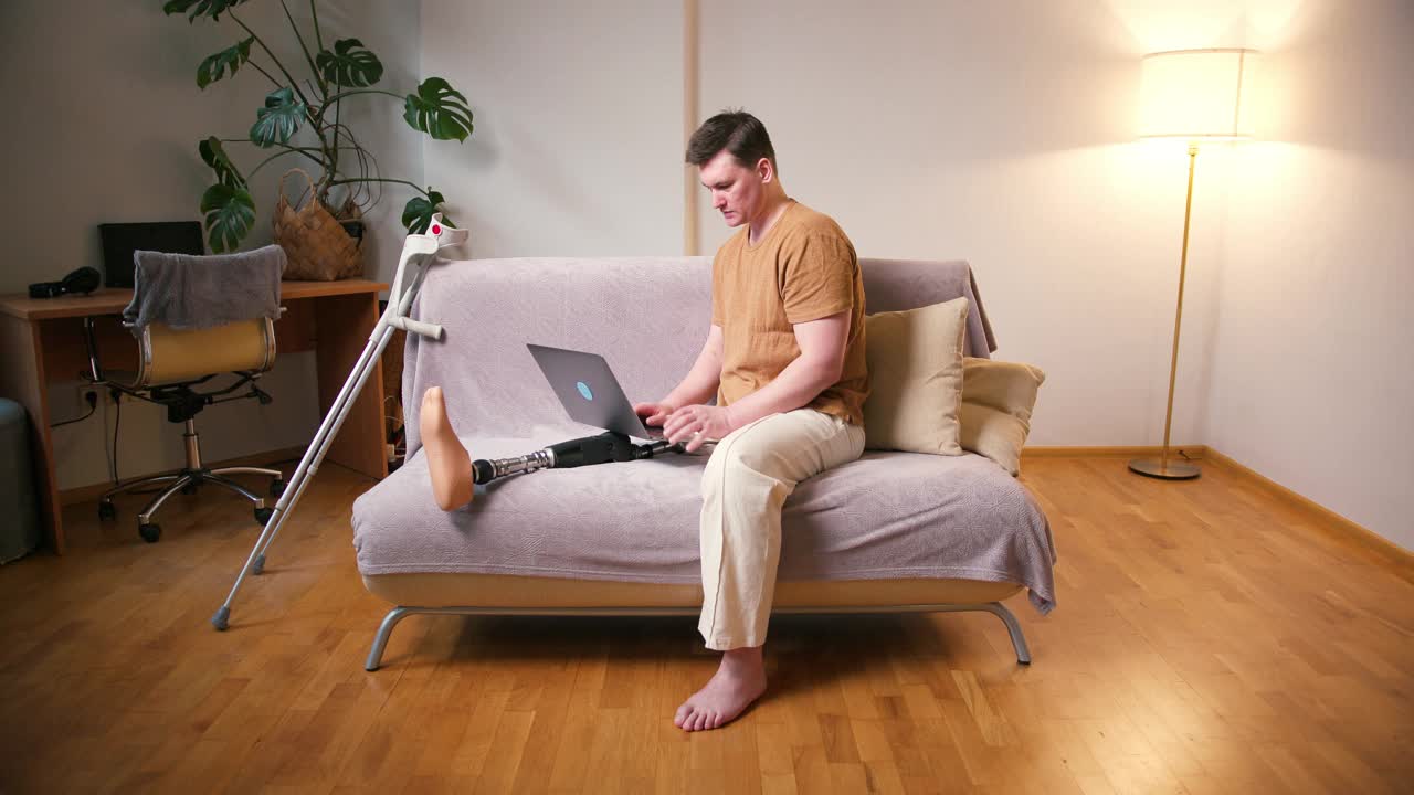 一名膝部以上假肢残疾的截肢者，在家里用笔记本电脑工作。截肢残障人士的日常生活视频素材