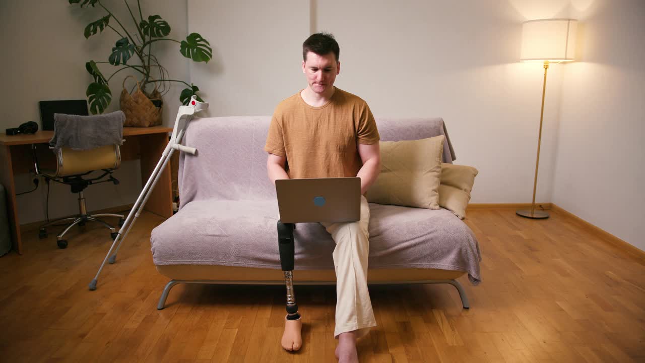 一名膝部以上假腿残疾的截肢者，在家中使用膝上型电脑安装经股腿假体人工装置。截肢残障人士的日常生活视频素材