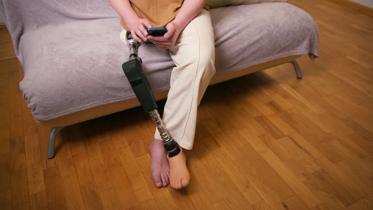 一名膝部以上假腿残疾的截肢者在家中使用智能手机安装经股腿假体人工装置。截肢残障人士的日常生活视频素材