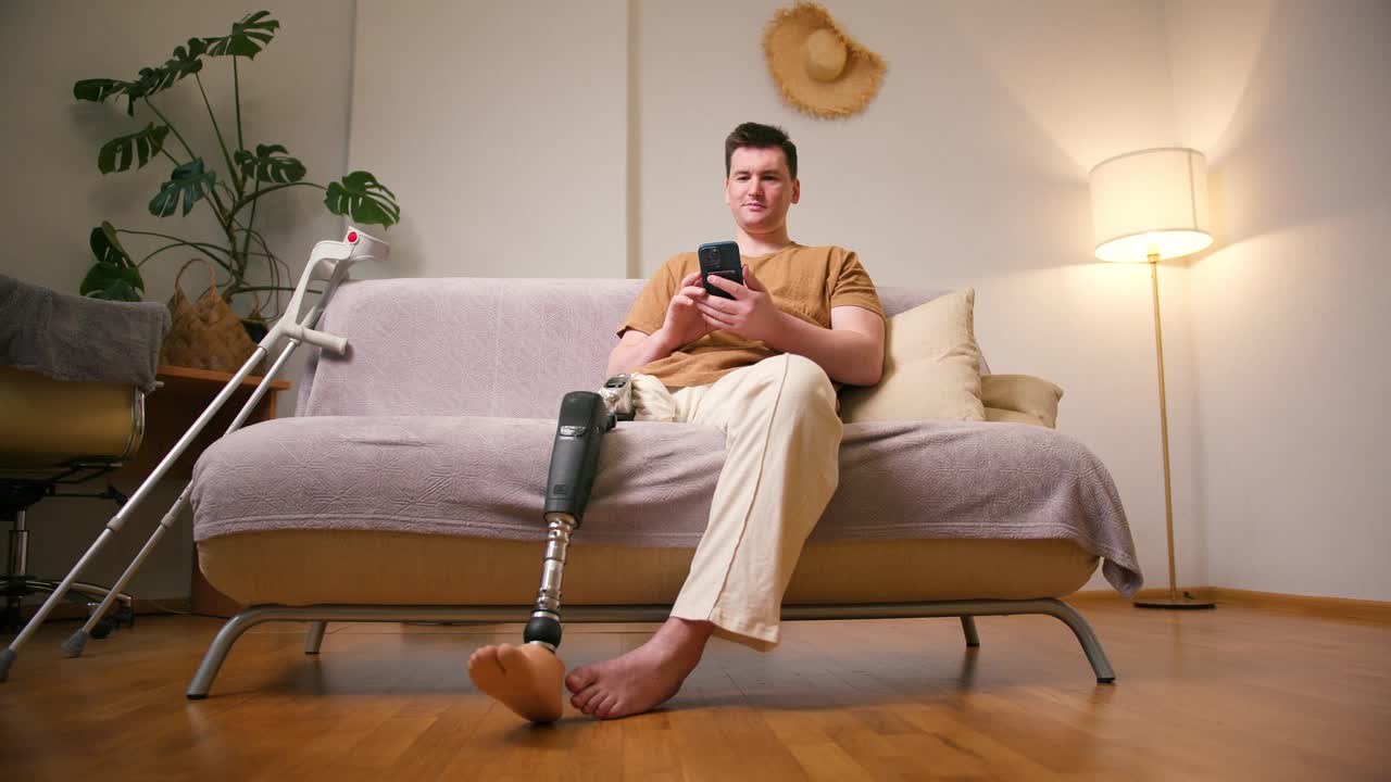 一名膝部以上假肢残疾的截肢者使用智能手机在家中进行视频通话。截肢残障人士的日常生活视频素材