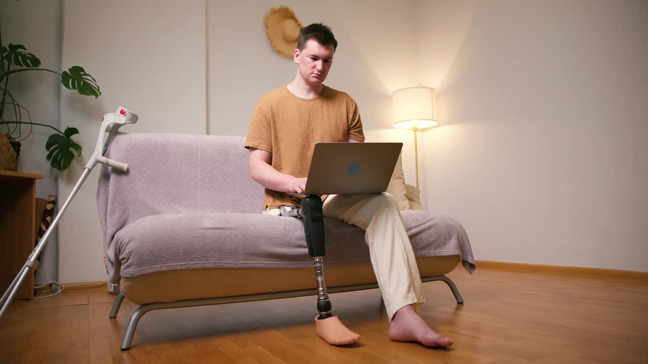 一名膝部以上假肢残疾的截肢者，使用膝上型电脑在家中进行视频通话。截肢残障人士的日常生活视频素材