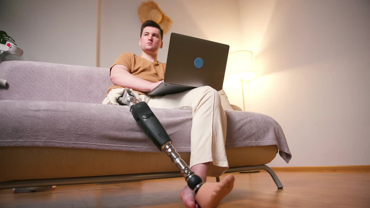 一名膝部以上假腿残疾的截肢者，在家中使用膝上型电脑安装经股腿假体人工装置。截肢残障人士的日常生活视频素材