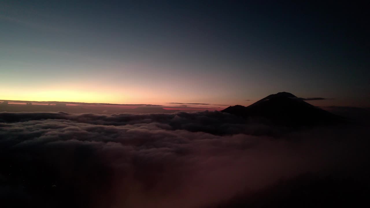 巴图尔火山在日落时笼罩在印尼巴厘岛的云海之上。无人机航拍视频素材