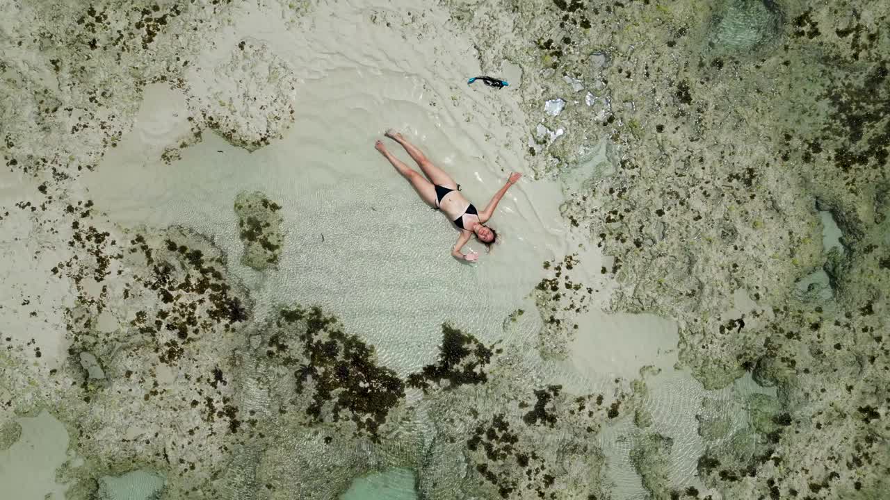 女孩独自在海边享受阳光。一名年轻女子头戴草帽，身穿黄色泳衣，躺在沙滩上视频下载