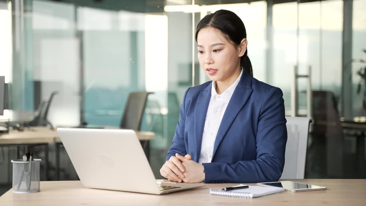 亚洲女商人坐在办公室用笔记本电脑进行视频通话。视频素材