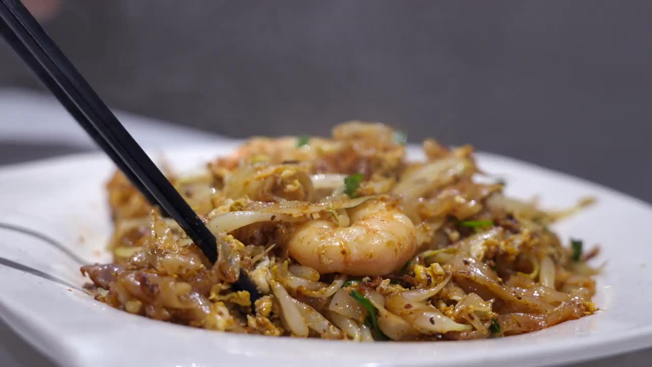 图为一名妇女正在享用“Char Koay Teow”，这是一种在马来西亚槟城很受欢迎的街头小吃，由炒米粉、扇贝、鸡蛋、豆芽、对虾、香葱、酱油和辣椒酱制成。视频素材