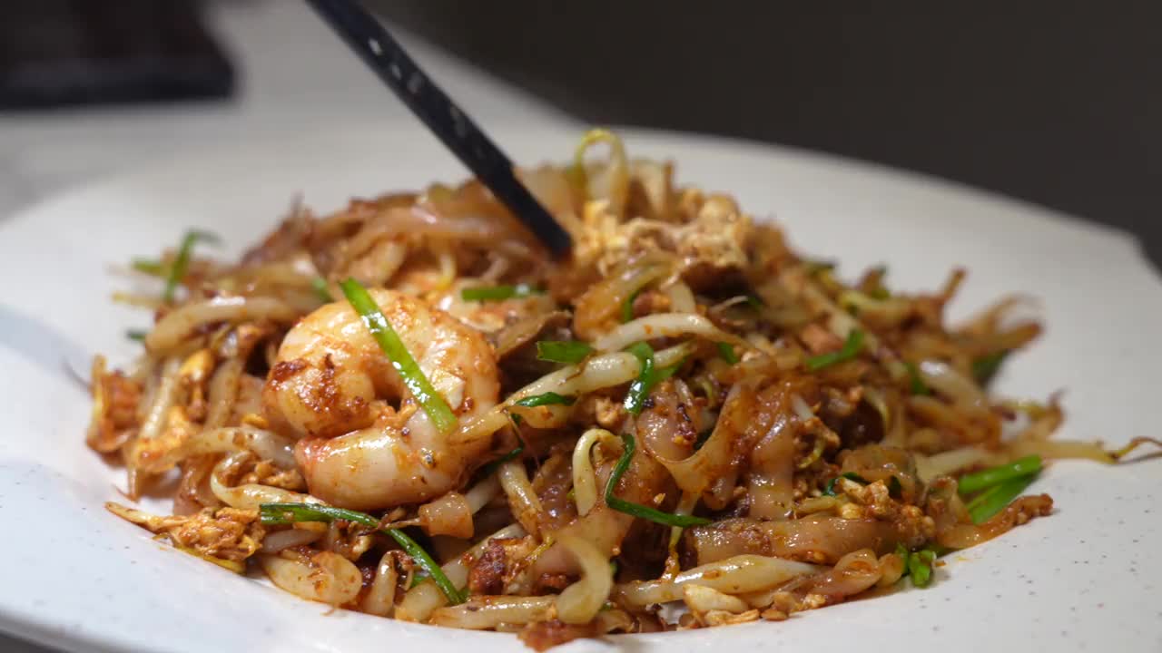 图为一名妇女正在享用“Char Koay Teow”，这是一种在马来西亚槟城很受欢迎的街头小吃，由炒米粉、扇贝、鸡蛋、豆芽、对虾、香葱、酱油和辣椒酱制成。视频素材