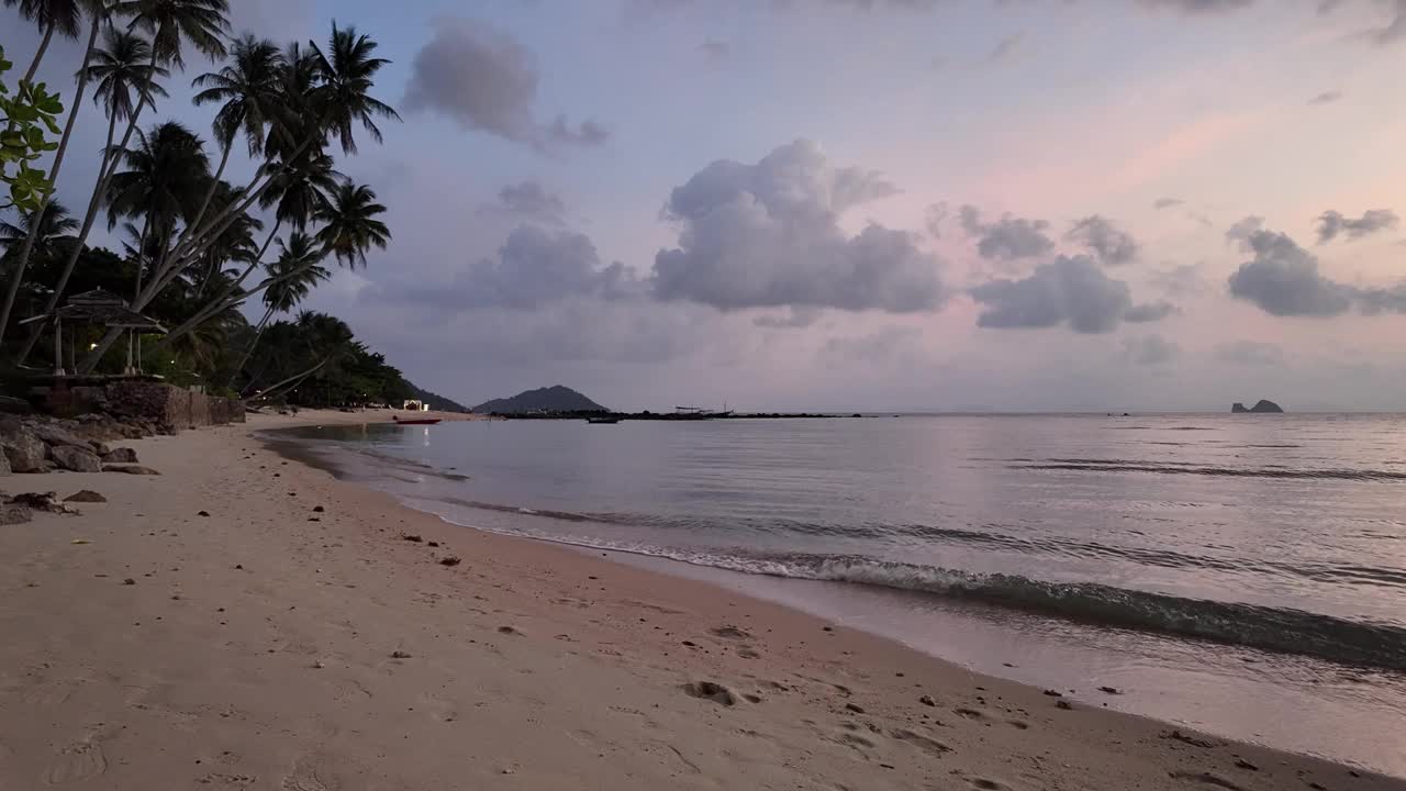 宁静的泰国苏梅岛宁静的海滩，在柔和的云和日落的温暖色调的背景下，温柔的海浪抚摸着海岸，旅游和度假的概念。视频素材