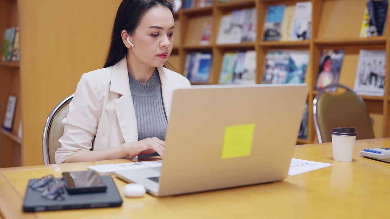 一个女人坐在桌子前，手里拿着一台笔记本电脑和一摞杂志视频素材