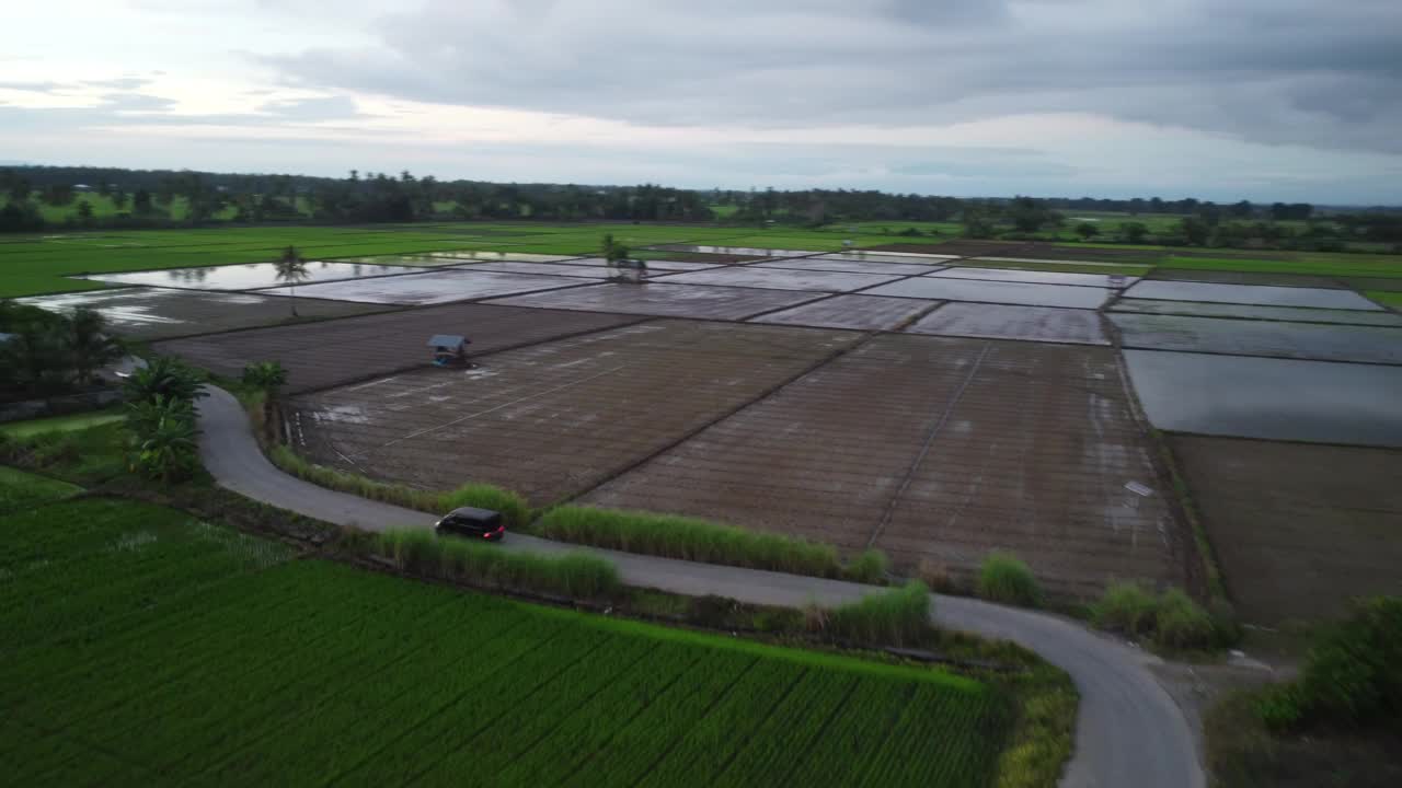 宁静的乡村风景，郁郁葱葱的田野，蜿蜒的道路和散落的建筑物，在多云的天空下。视频下载