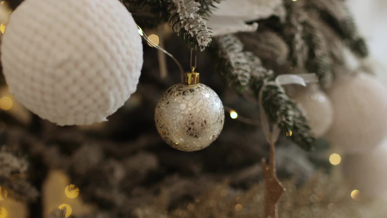 近距离观察美丽的冷杉树枝上闪闪发光的白色小玩意或球，金色的圣诞装饰品和灯。节日的背景。圣诞树上的装饰。喜庆新的2025年。副本的空间。视频下载