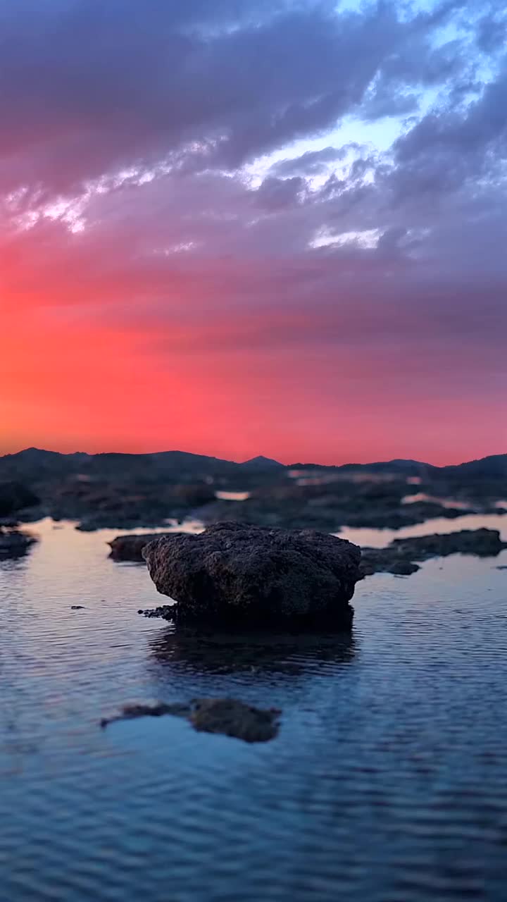 垂直视图的岩石海岸与宁静的大海对红色多云的天空背景在日落视频素材