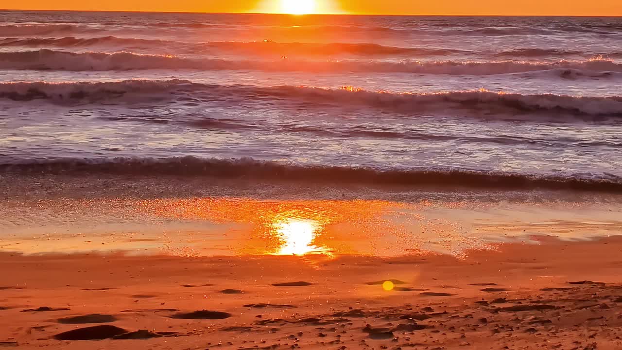 夕阳把拍打在沙滩上的波浪染成了橙色。慢镜头。视频素材