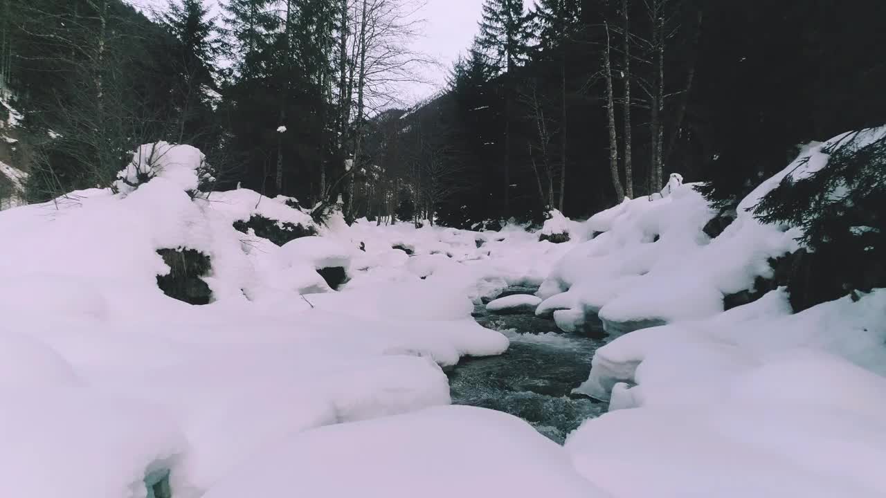 4K无人机在雪天跟随河流穿过森林的视频视频下载