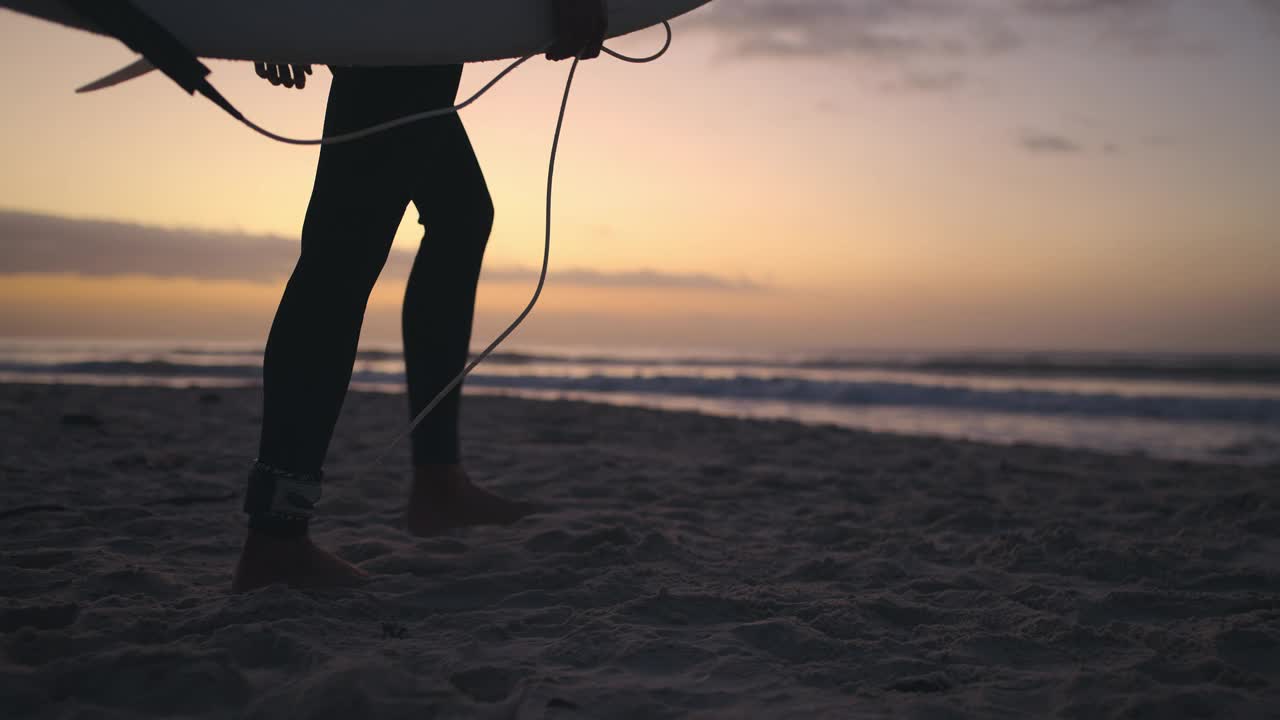 男人，冲浪和在落潮时在海边漫步，爱好或在大自然中户外运动。穿着冲浪板或潜水服在日出的海滩或海岸边进行极限运动的男性视频素材