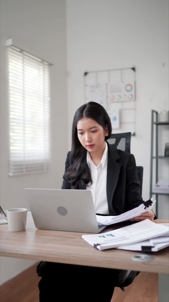 这位专注的年轻亚洲女商人正在办公桌上的笔记本电脑上搜索和阅读文件，准备写项目报告视频素材