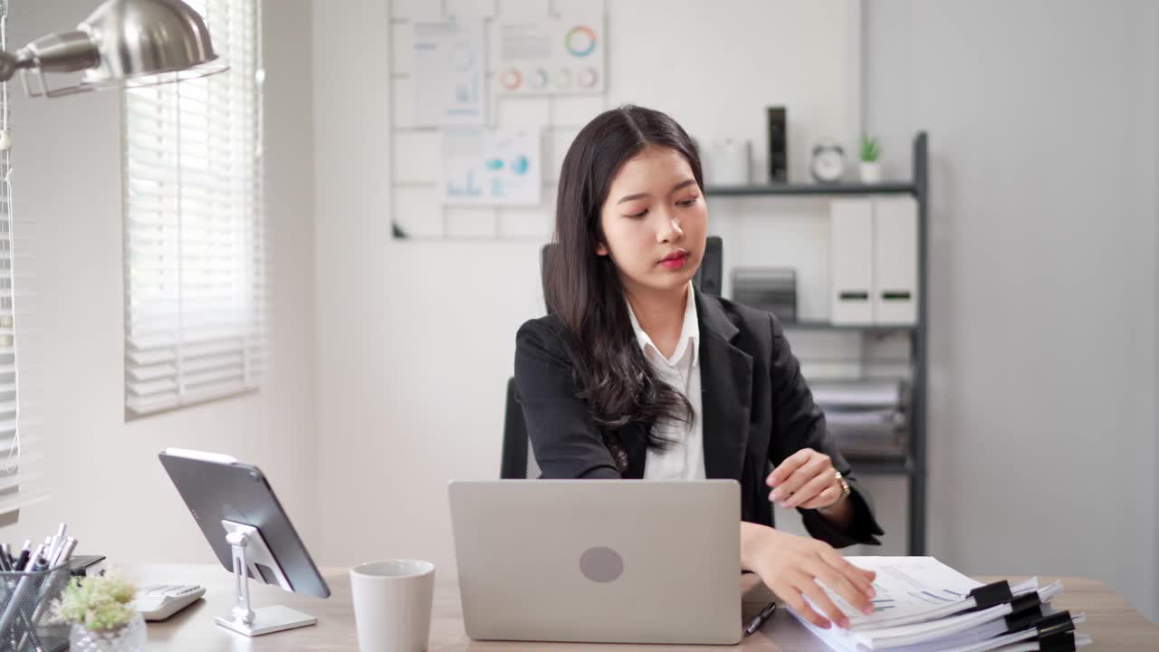 这位专注的年轻亚洲女商人正在办公桌上的笔记本电脑上搜索和阅读文件，准备写项目报告视频素材