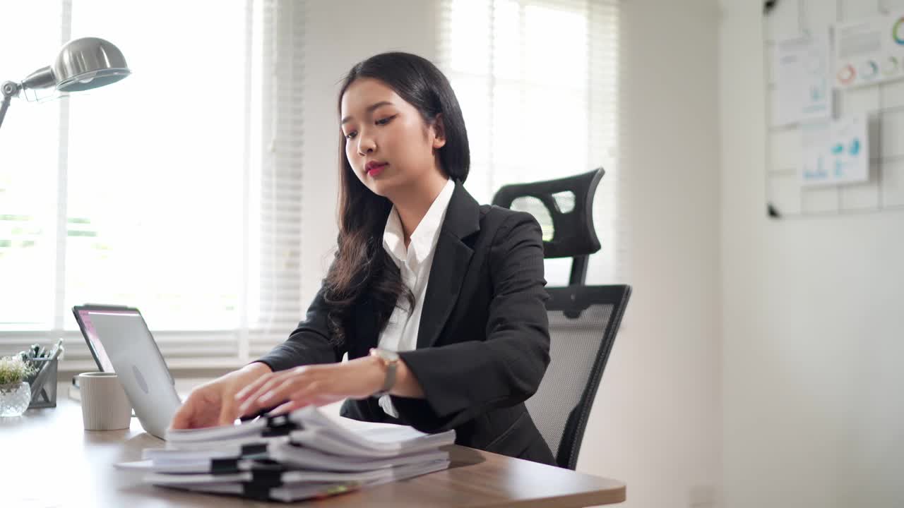 这位专注的年轻亚洲女商人正在办公桌上的笔记本电脑上搜索和阅读文件，准备写项目报告视频素材