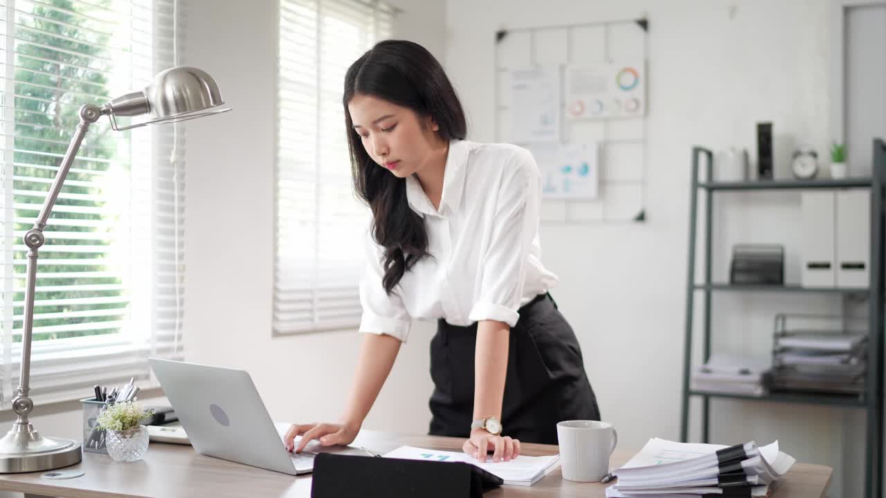 这位专注的年轻亚洲女商人正在办公桌上的笔记本电脑上搜索和阅读文件，准备写项目报告视频素材