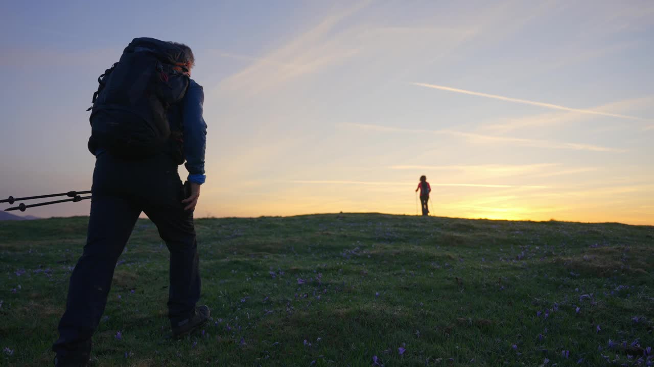 夕阳下，在Velika Planina山徒步旅行时，成熟男人走向女人并拥抱的后视图跟踪镜头视频素材