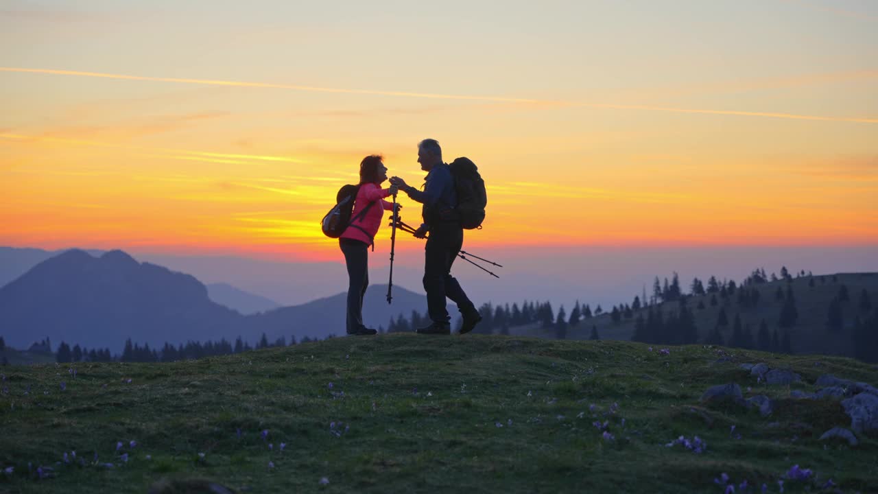 兴奋的成熟夫妇背着背包和登山杖拥抱在日落时庆祝成功视频素材