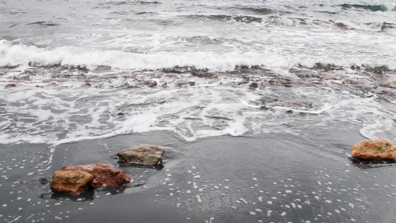 海浪冲击着黑色的海滩，带着铁屑视频下载