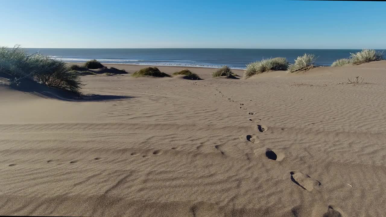 宁静的海滩上的沙丘和温柔的海浪脚印。4K镜头视频下载