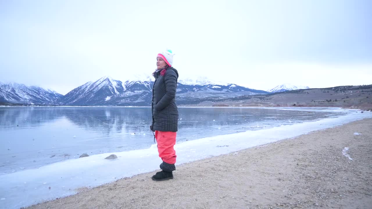 摄影师望着冰封的湖面，背景是雪山视频素材