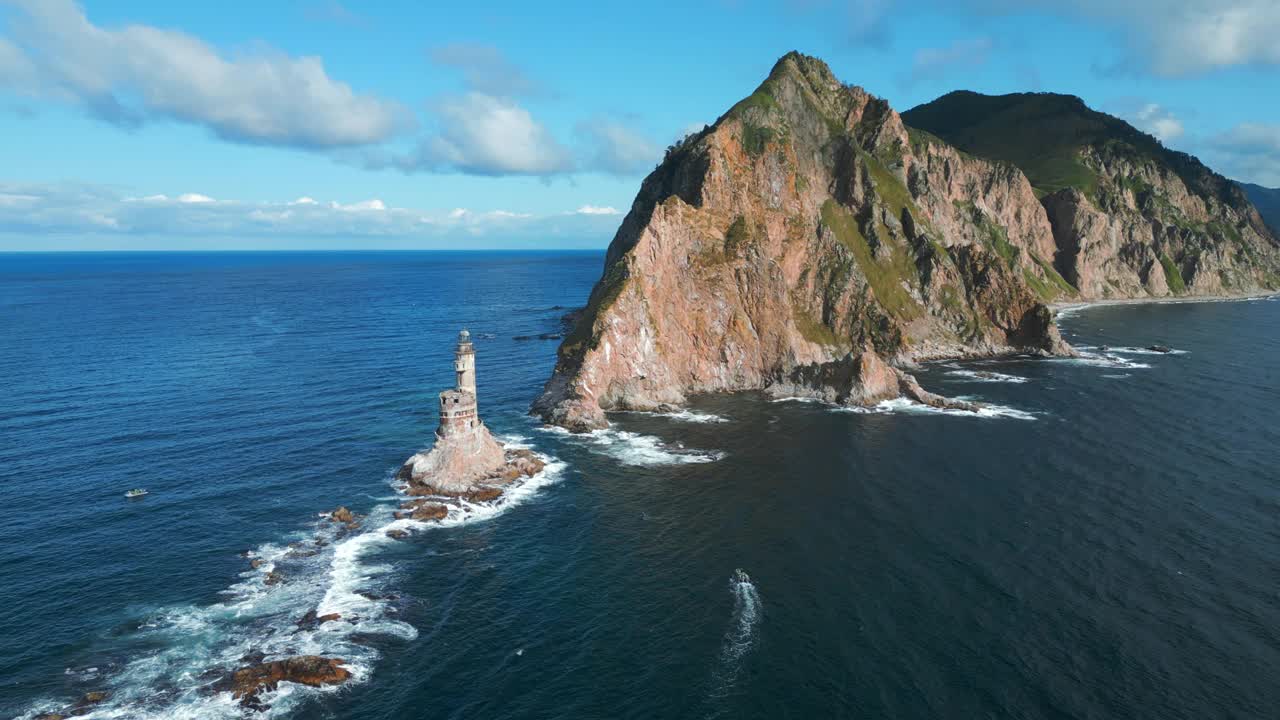 俯瞰美丽的岩石岬角和灯塔。夹。岩石岬角和灯塔的电影景观与海浪。在阳光明媚的夏日，海上的岩石岬角和废弃的灯塔视频素材