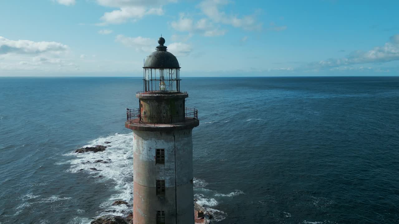 在阳光明媚的日子里，海上废弃灯塔的俯视图。夹。被遗弃的灯塔矗立在波涛汹涌的蓝色大海上。美丽的灯塔在海浪撞击岩石的背景下视频素材