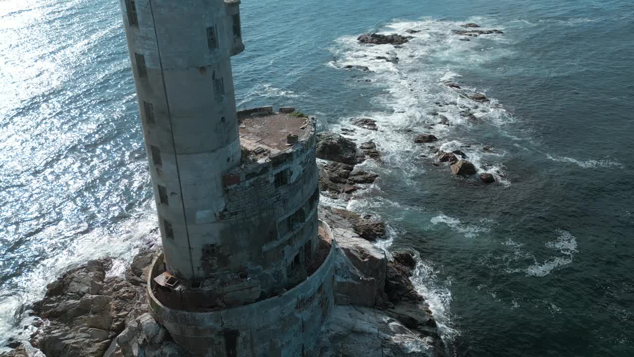 在阳光明媚的日子里，海上废弃灯塔的俯视图。夹。被遗弃的灯塔矗立在波涛汹涌的蓝色大海上。美丽的灯塔在海浪撞击岩石的背景下视频素材