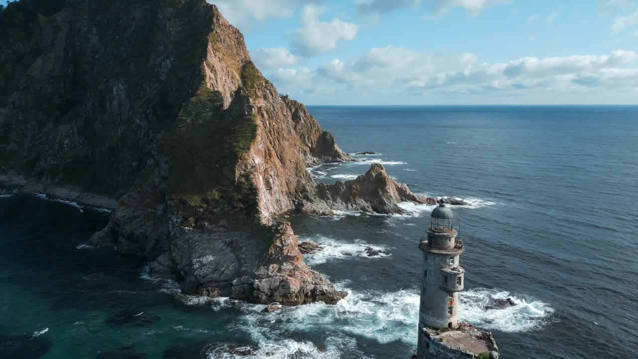 俯瞰美丽的岩石岬角和灯塔。夹。岩石岬角和灯塔的电影景观与海浪。在阳光明媚的夏日，海上的岩石岬角和废弃的灯塔视频素材