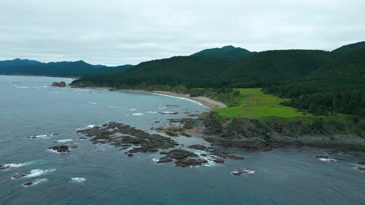 海岸外的石礁与绿色的森林和岩石的俯视图。夹。美丽的波浪在珊瑚礁海岸与绿色森林的山。北方的景观，绿色的山脉和岩石在阴天的海岸视频素材