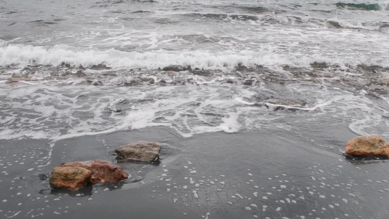 海浪冲击着黑色的海滩，带着铁屑视频素材