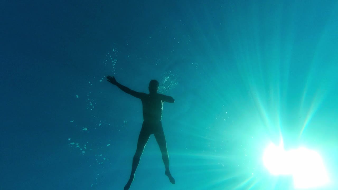 水下拍摄。一个人漂浮在水面上，以天空和太阳为背景，看着海底和鱼。视频素材