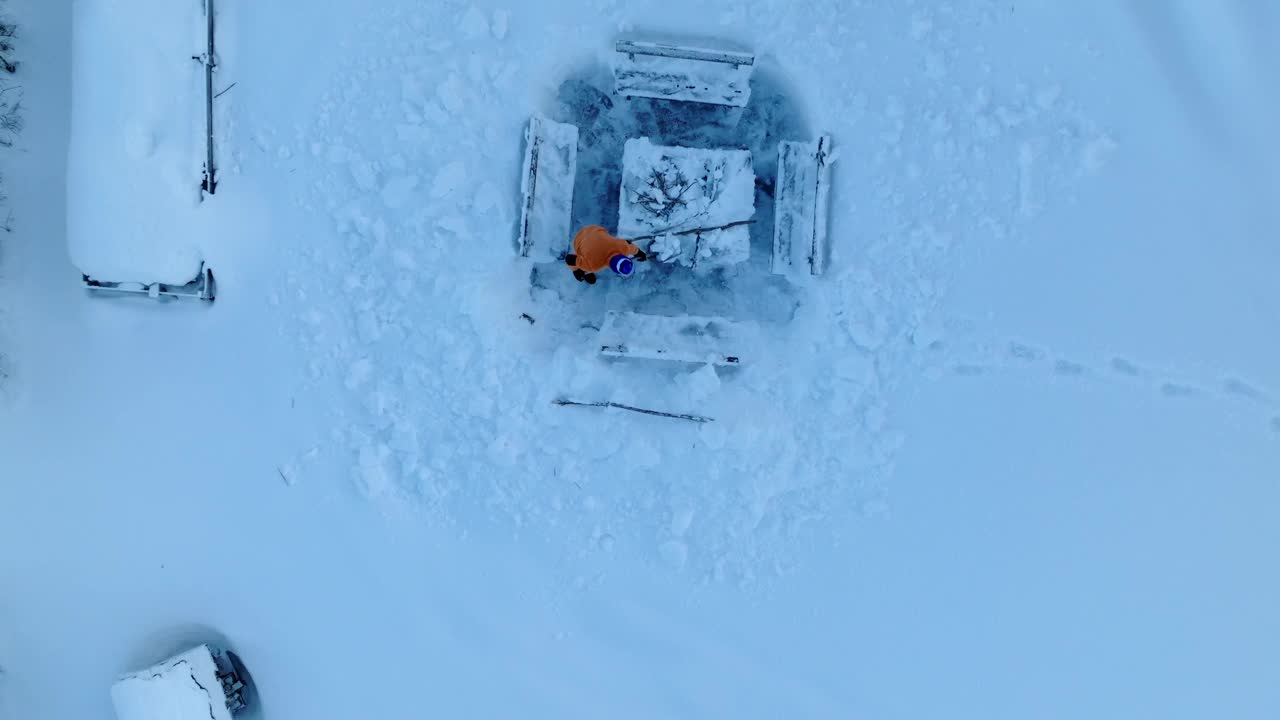 一名身穿橙色夹克的男子站在长凳旁清理积雪，鸟瞰图视频下载