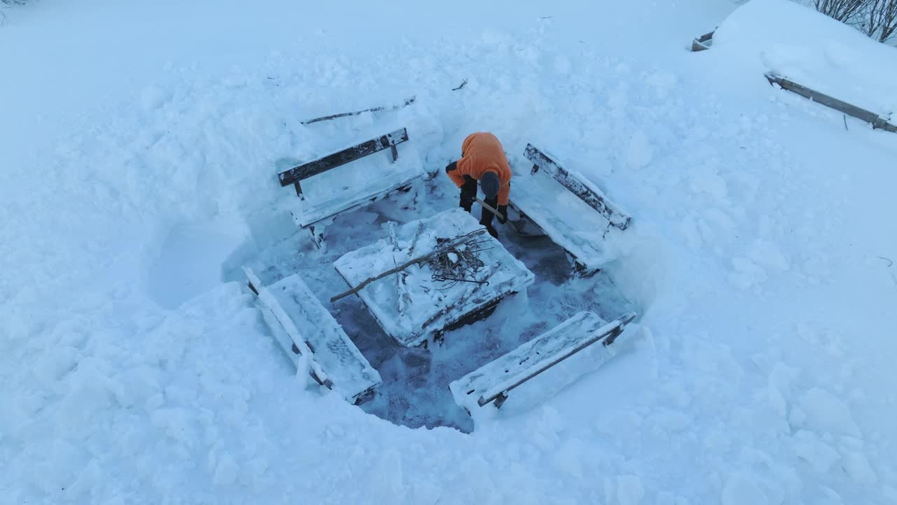 一名身穿橙色夹克的男子正站在烤炉上的木凳下清理积雪视频素材