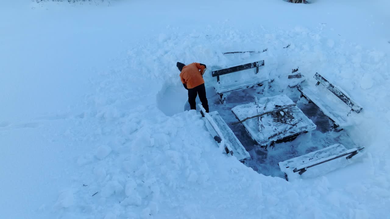 一名身穿橙色夹克的男子站在那里，用雪楼梯进入烧烤灶。近距离航拍视频视频下载