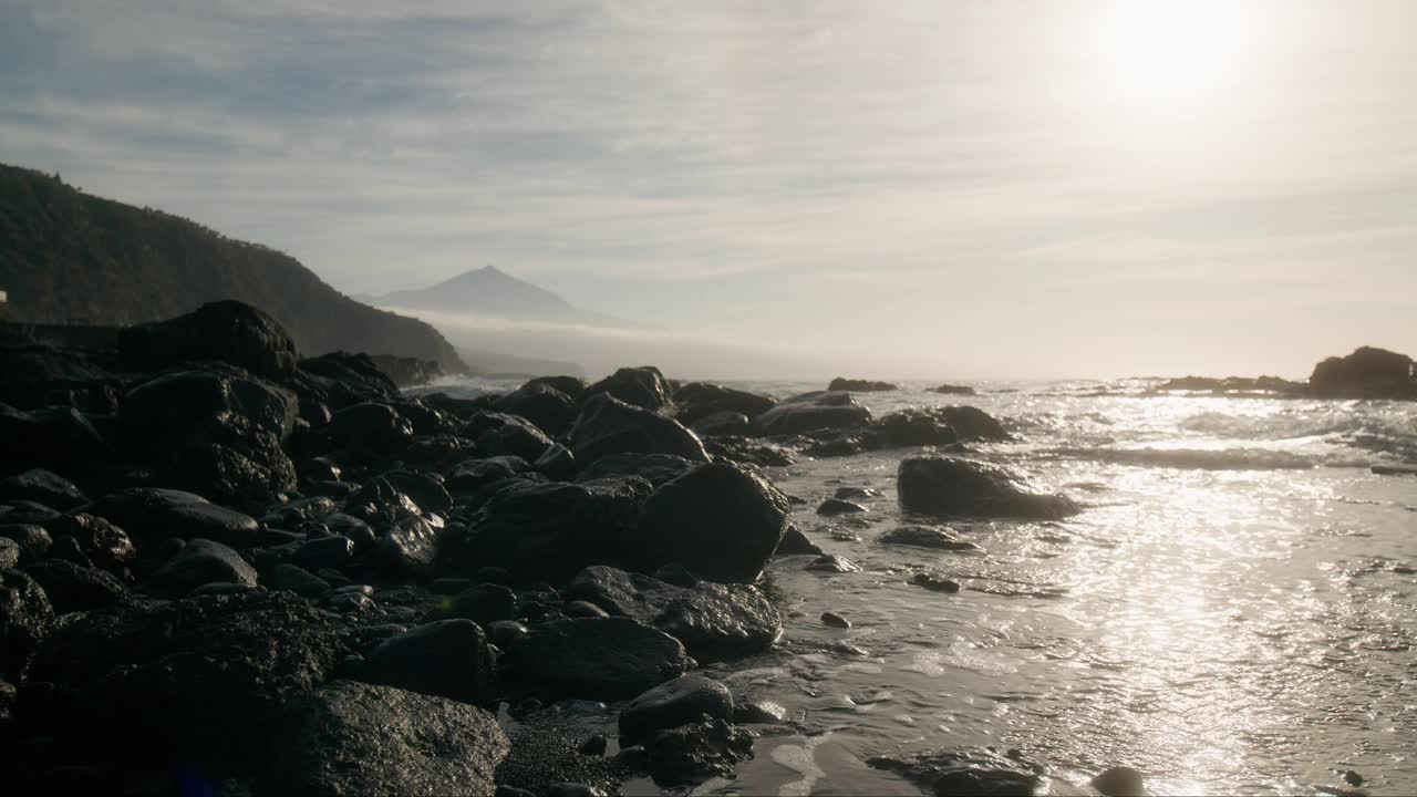 空灵的黑色沙滩黄昏与远处的Pico del Teide山，朦胧的岩石与黎明平滑的波浪，加那利群岛的特内里费岛视频素材