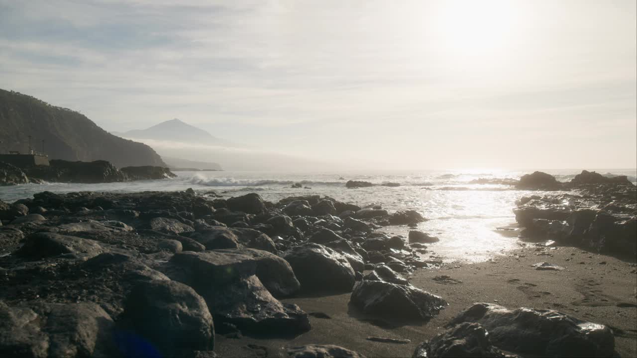 空灵的黑色沙滩和远处的Pico del Teide山，朦胧的岩石和黎明时平稳的海浪，加那利群岛的特内里费岛视频素材